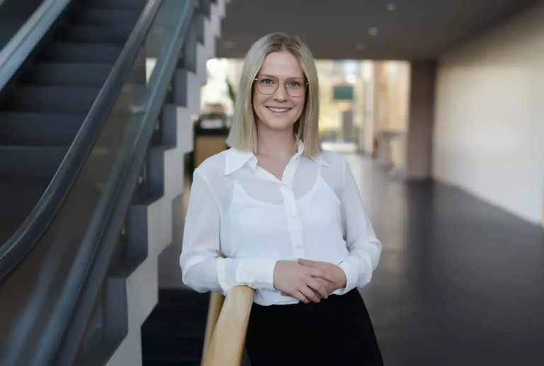 Anna Schmid von Carthago mit Brille lächelt in modernem Treppenhaus in die Kamera.