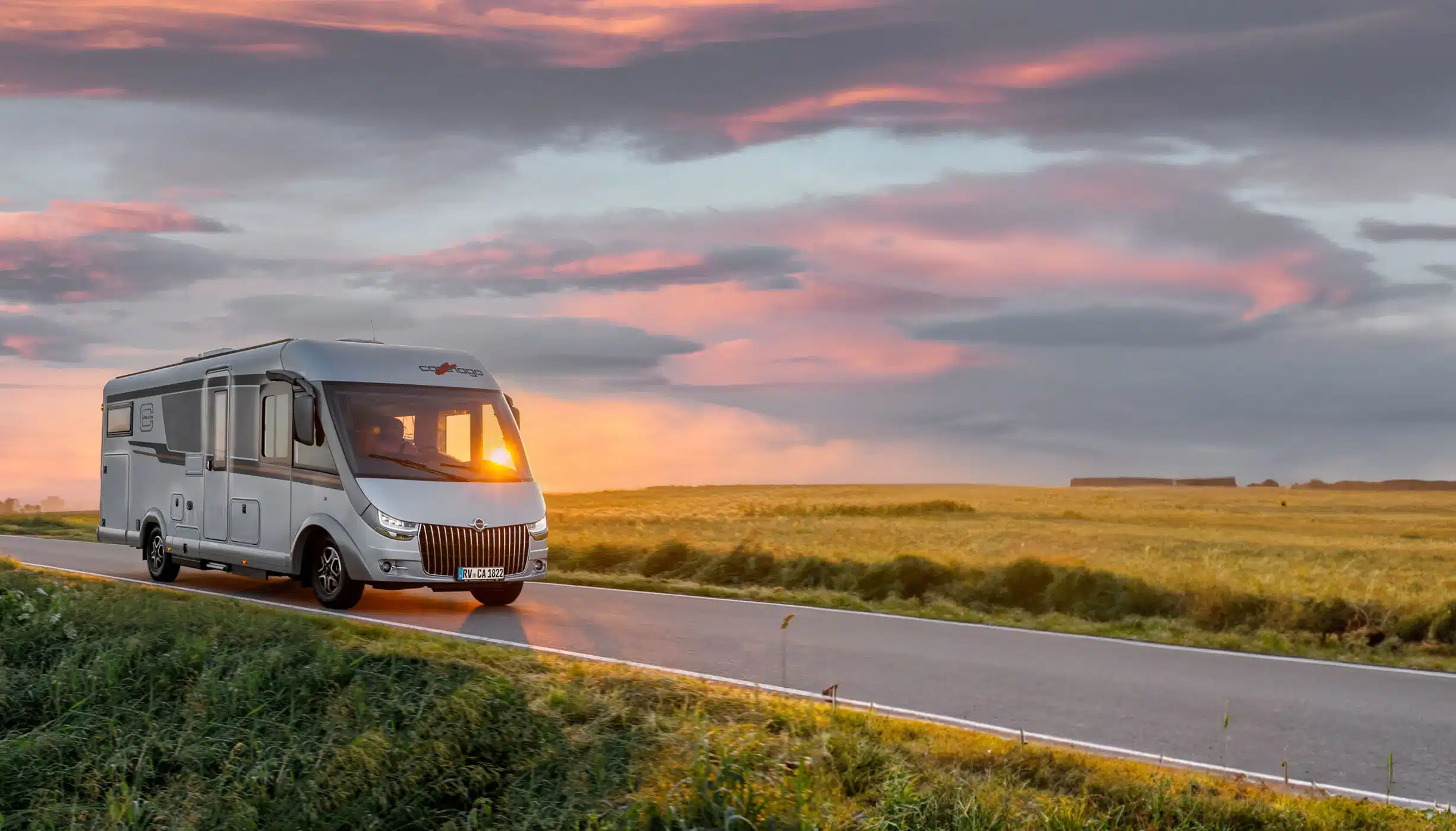Ein integriertes Reisemobil von Carthago fährt über eine leere Landstraße inmitten weiter Felder.