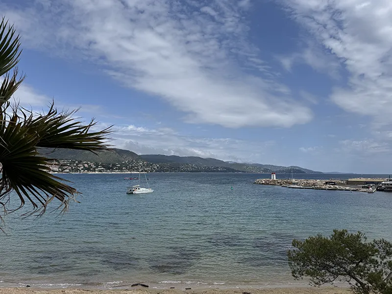 Ein einsames Segelboot liegt ruhig vor Anker, während sich das glitzernde Meer bis zum Horizont unter einem teils wolkigen Himmel erstreckt.