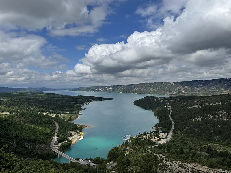 Panoramablick auf einen türkisblauen See, umgeben von bewaldeten Hügeln und dramatischer Wolkenkulisse – Natur in ihrer beeindruckenden Weite.