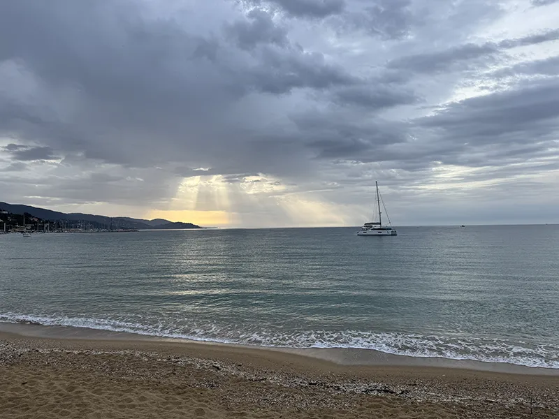 Sonnenstrahlen brechen durch die dichte Wolkendecke und tauchen das Meer in ein sanftes Licht – ein stiller Moment am Horizont.