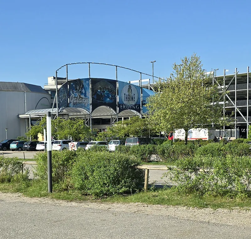 Blick auf den Eingang der Therme Erding mit dem Galaxy Rutschenparadies und dem angrenzenden Parkhaus an einem sonnigen Tag.