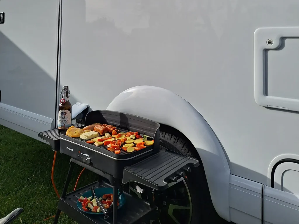 Fleisch und Gemüse auf einem Grill, der vor dem Malibu Reisemobil steht